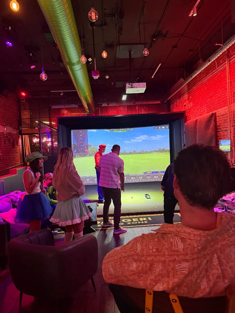 Guests playing at the Full Swing simulator bay under neon lights