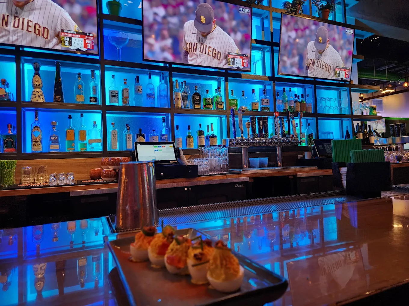 The Swing Social bar with wall of TVs showing San Diego Padres and a spread of deviled eggs