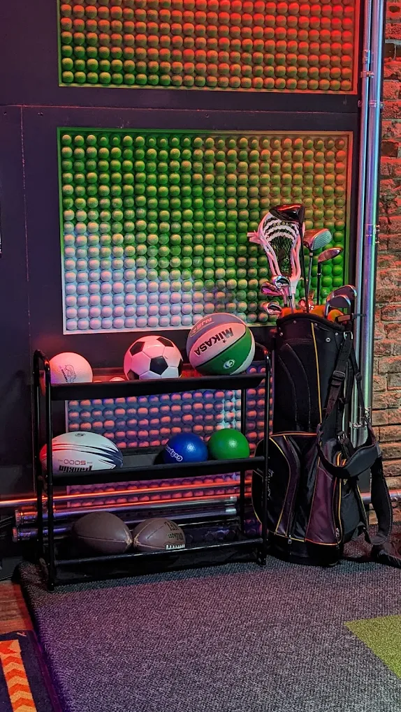 Rack of balls and golf clubs against the tennis-ball wall